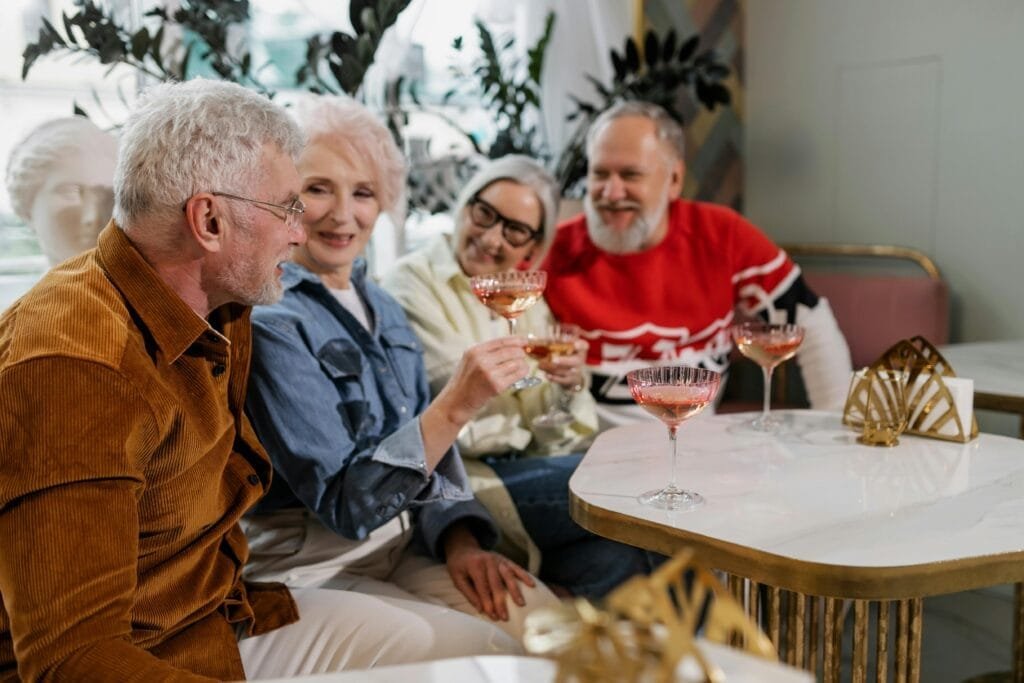 Senioru draugi bauda jautru kopā sanākšanu telpās, daloties dzērienos un smieklos.